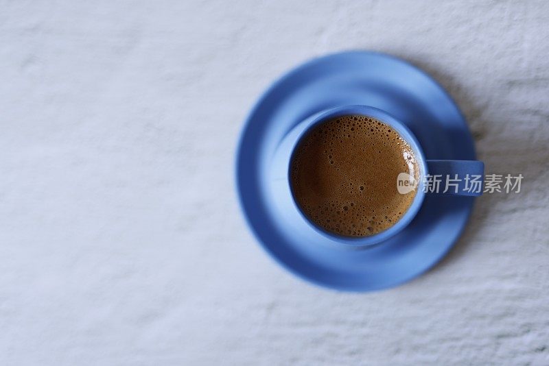 在浅灰色的混凝土地板上，蓝色陶瓷杯里的土耳其起泡咖啡