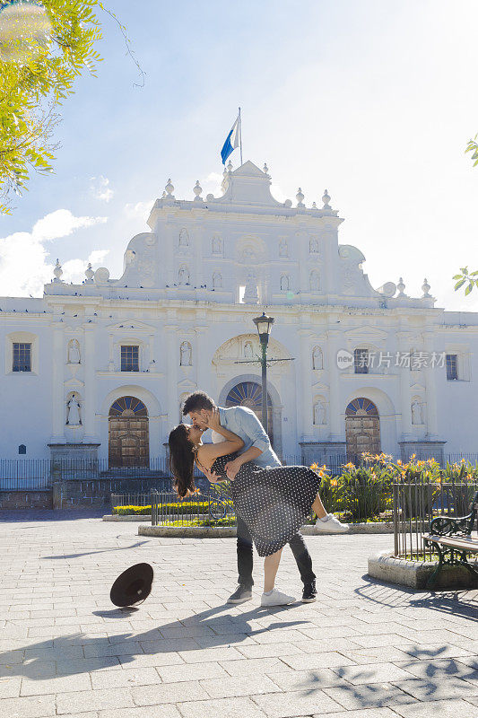 一对西班牙情侣在危地马拉安提瓜的圣何塞大教堂前相爱，年轻的游客们在阳光明媚的日子里享受着他们在这座殖民城市的假期，情侣们在公园里接吻