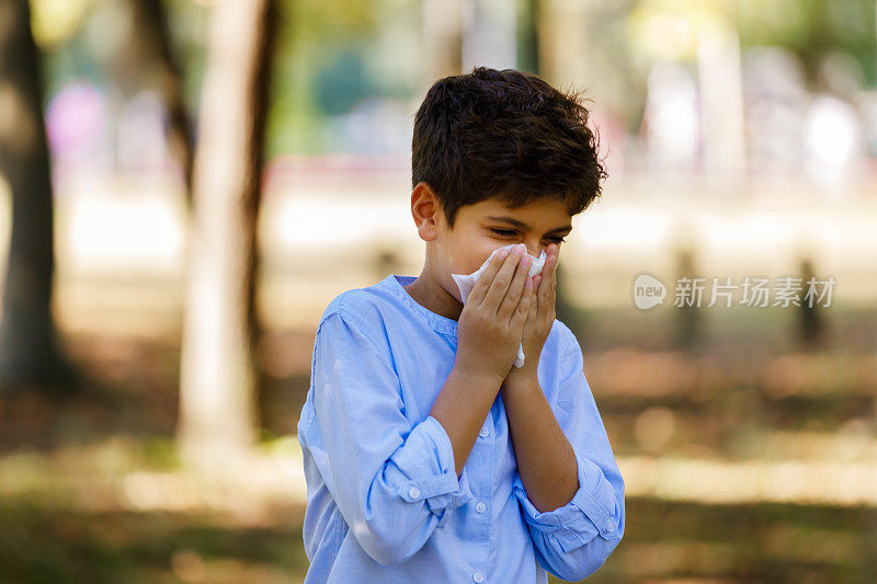 患季节性流感的男孩在公园里散步，用纸巾咳嗽。