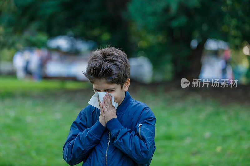 季节性过敏的病男孩用纸巾擤鼻子。