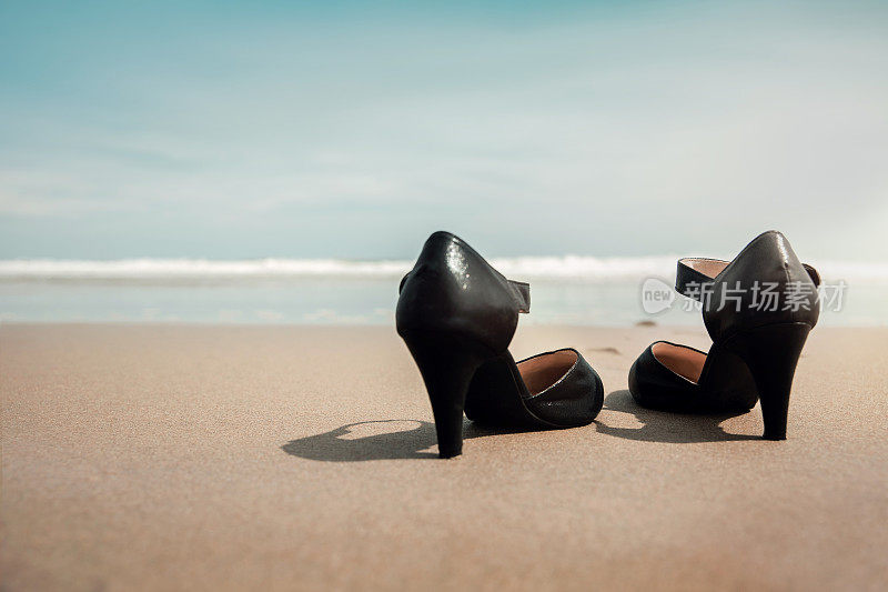 平衡工作与生活的理念。女商人脱掉工作鞋，把它留在沙滩上