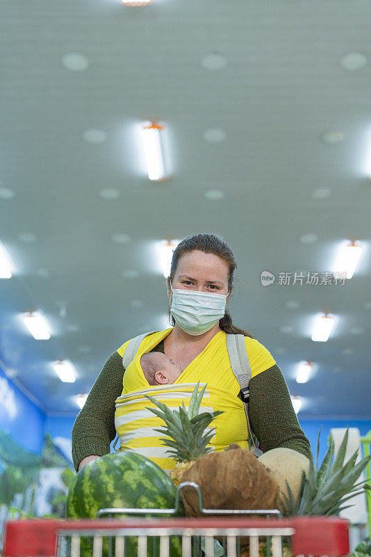 年轻的妇女抱着她的孩子在超市的水果和蔬菜选择他们的食物时看着相机的肖像