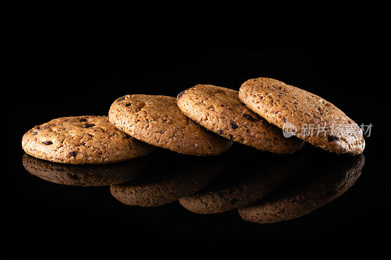 燕麦饼干和巧克力片是孤立的黑色背景与反射。大量棕色圆形自制饼干躺在反射表面，特写