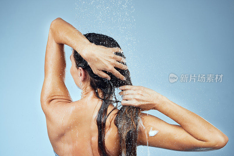 工作室拍摄的一个迷人的年轻女子洗她的头发，同时洗澡在蓝色的背景