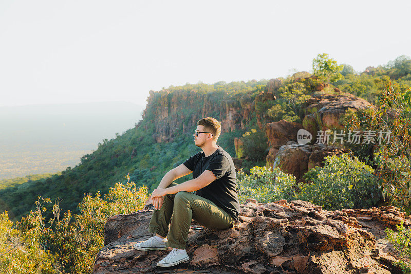 一名男性旅行者在纳米比亚的山顶上凝视着日落美景