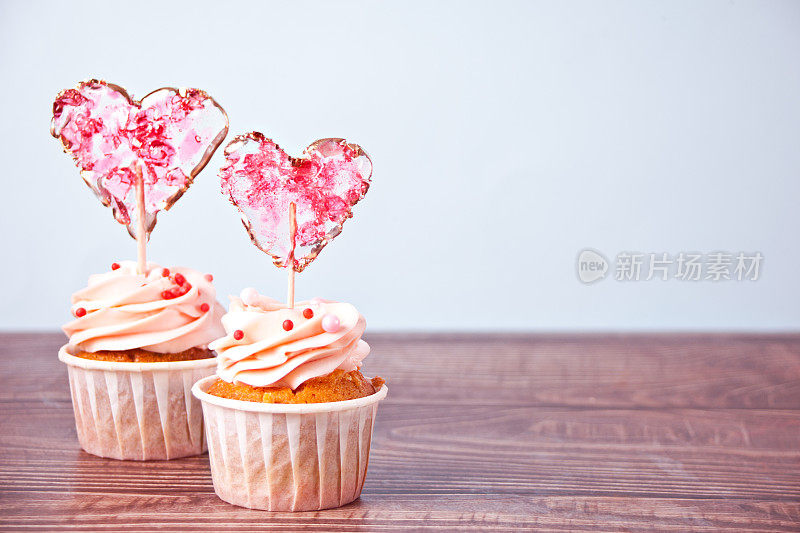 情人节纸杯蛋糕，奶油芝士糖霜，装饰心形糖果棒棒糖木制背景