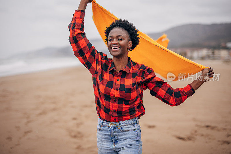 年轻女子在海滩上跑步，在风中有围巾的乐趣