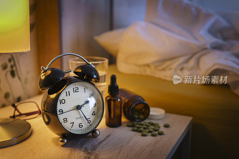 失眠与睡眠障碍的概念。床头柜上有闹钟和安眠药。