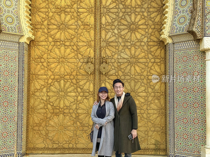 在摩洛哥菲斯，一对亚洲中国游客站在皇宫门口看镜头。