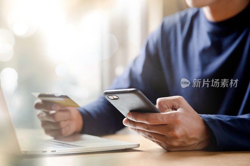 男子手持信用卡，在家使用智能手机网上购物电子商务网上银行消费在家工作的概念。