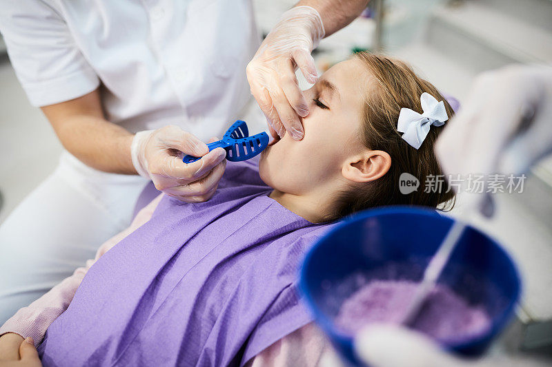 牙科诊所预约期间，牙科医生为小女孩的牙齿涂上牙模的特写镜头。