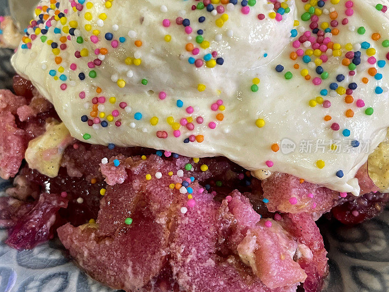 全帧图像的图案蓝色盘子与小蛋糕部分顶部与鲜奶油浇头彩虹多色糖洒，层海绵蛋糕，蛋奶沙司和草莓果冻，抬高视图