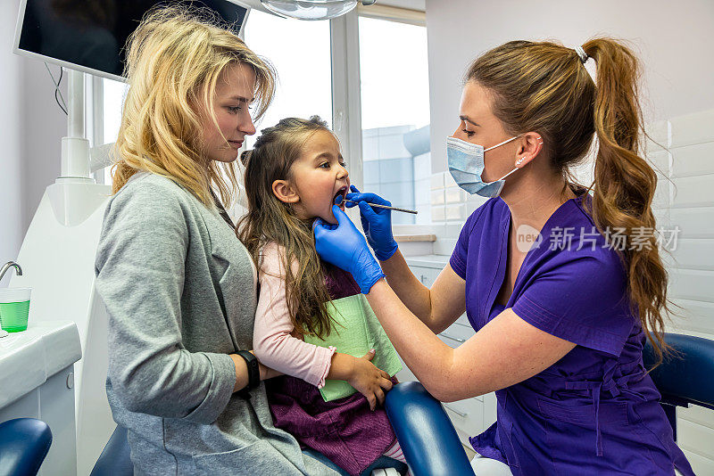 女牙医检查病人的牙齿，而她的母亲在牙科诊所支持她。