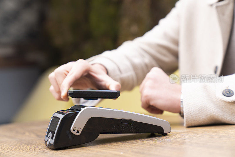 特写:一名男性在咖啡馆用智能手机用信用卡非接触式支付支付账单，在卡机上扫描。电子支付。银行和科技