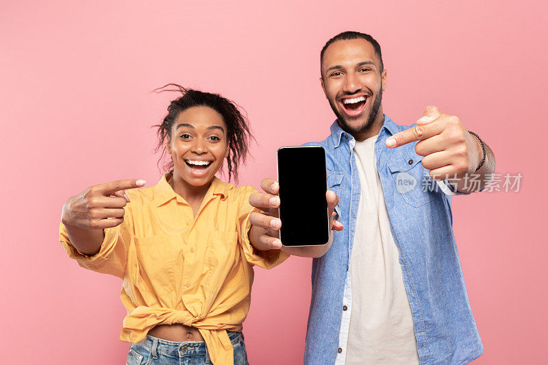 使用这个新的应用程序。兴奋的黑人夫妇指着空白屏幕的智能手机，为设计做模型