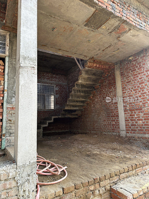 红砖两层楼带楼梯的建筑内部图像，印度建筑工地在住宅区，部分建成两层楼，重点关注前景
