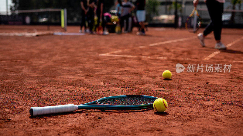 两个网球和网球拍放在红土场上，前景是网球运动员，背景是水平网球