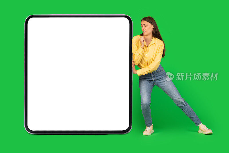 女人在绿色背景上推着巨大的方形空小工具屏幕