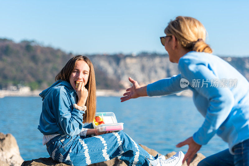 阳光明媚的冬日，母亲和十几岁的女儿在岩石海滩上野餐的快乐时刻