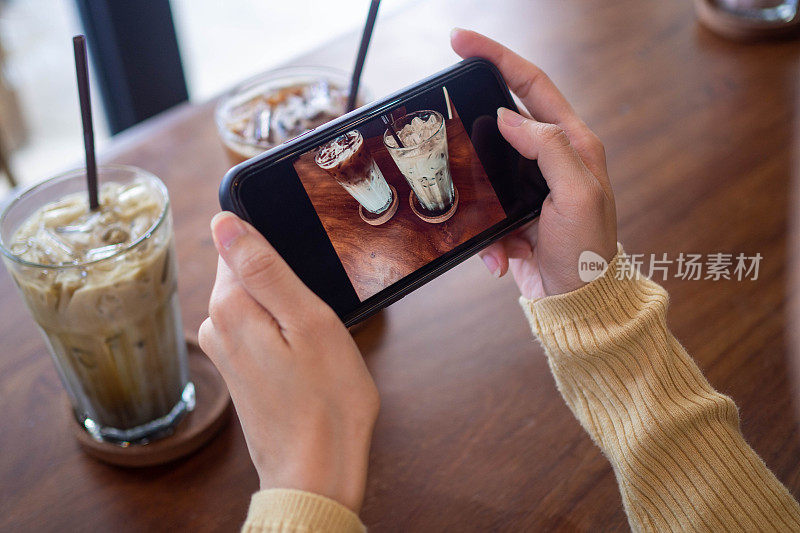 一位女士正在用智能手机给咖啡拍照。女性通过拍照在社交媒体上发布或分享受欢迎的菜肴。
