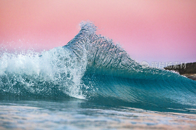 蓝色的海浪在傍晚的淡粉色的天空中闪烁