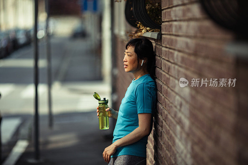 一名年轻的日本女子在城市里运动后休息片刻，喝了点水