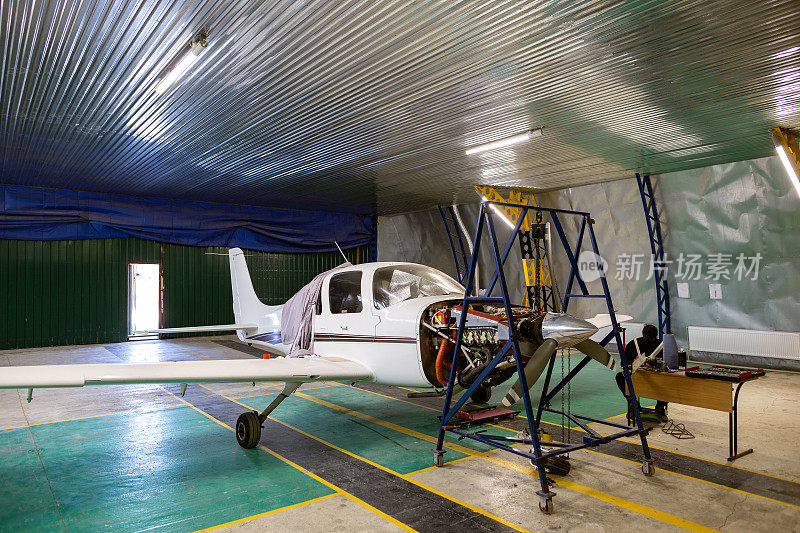 机库是一家小型汽车修理店。轻型单发飞机，需要维修发动机。飞机发动机悬挂在链式起重机上。