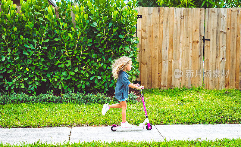 一个小学小女孩穿着校服在郊区的人行道上骑着摩托车