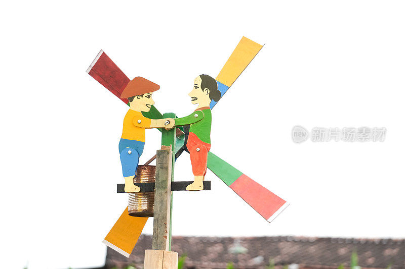 一个小型风力涡轮机——五颜六色的木制风车与两个农民的身影握手。印尼风车螺旋桨玩具，适合儿童和家庭装饰。空白复制文本空间。