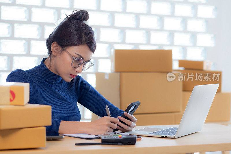 年轻的亚洲女性在网上为卖家提供送货服务，而女性在家里看智能手机，在文件上写客户的订单，在线送货，自由职业者做小生意。