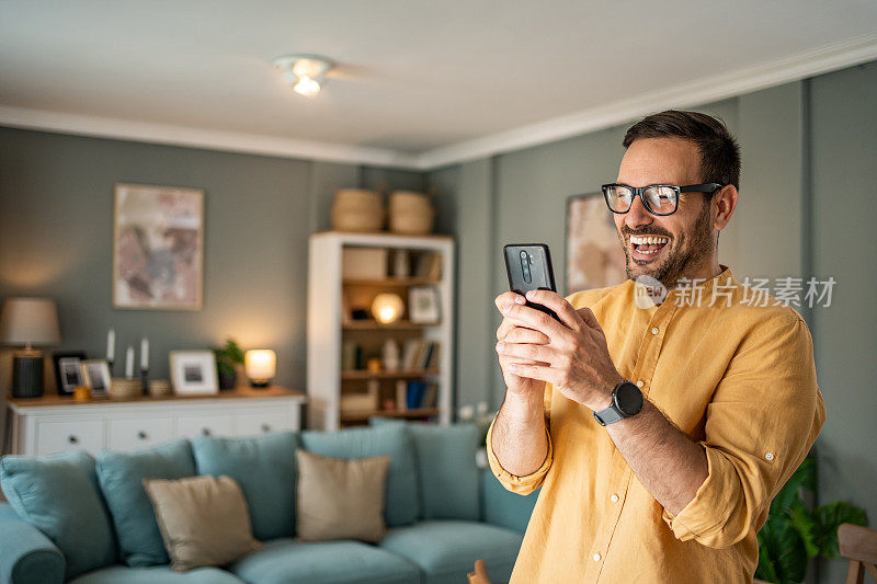 英俊的中年白人男子在家里的客厅用手机自拍或打视频电话
