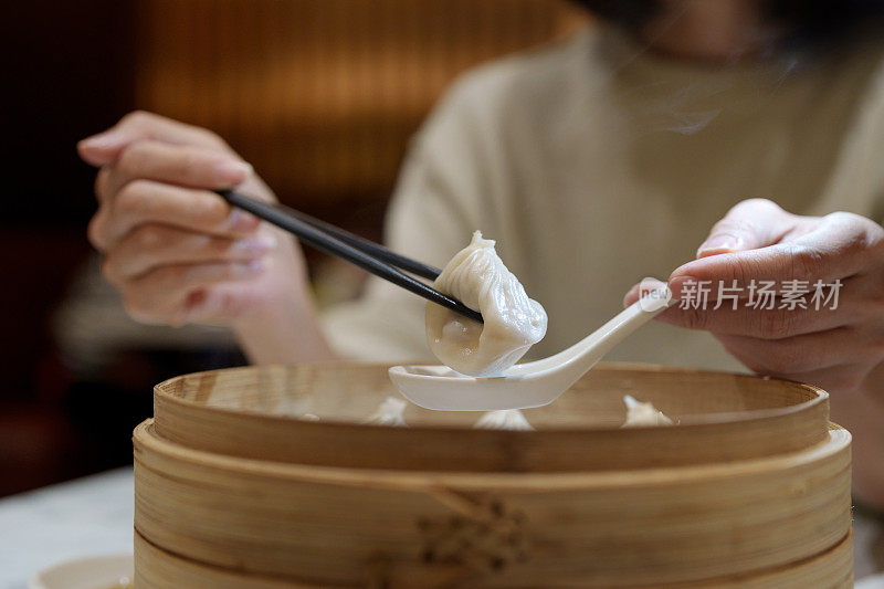 用筷子夹着小笼包的女性手特写，这是一种放在竹制蒸笼里的中国传统食物。