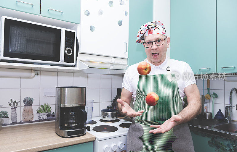 一名戴着厨师帽的白人男子在家庭厨房里摆弄红苹果。