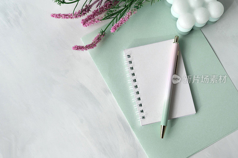 空白的笔记本纸、笔、春花、淡蜡绿的纸文具，大理石中性桌面背景，优雅女性化的商务工作空间，规划理念，平铺