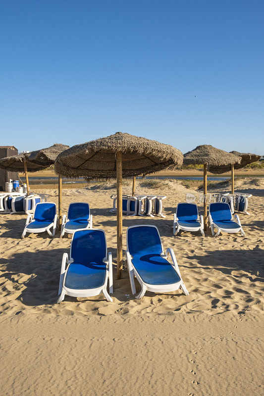 美丽的夏日西班牙海岸景观，几个日光浴躺椅，日光浴躺椅和遮阳伞。金色细沙，地平线海景，蓝天，平静放松。鼓舞人心的度假景观。