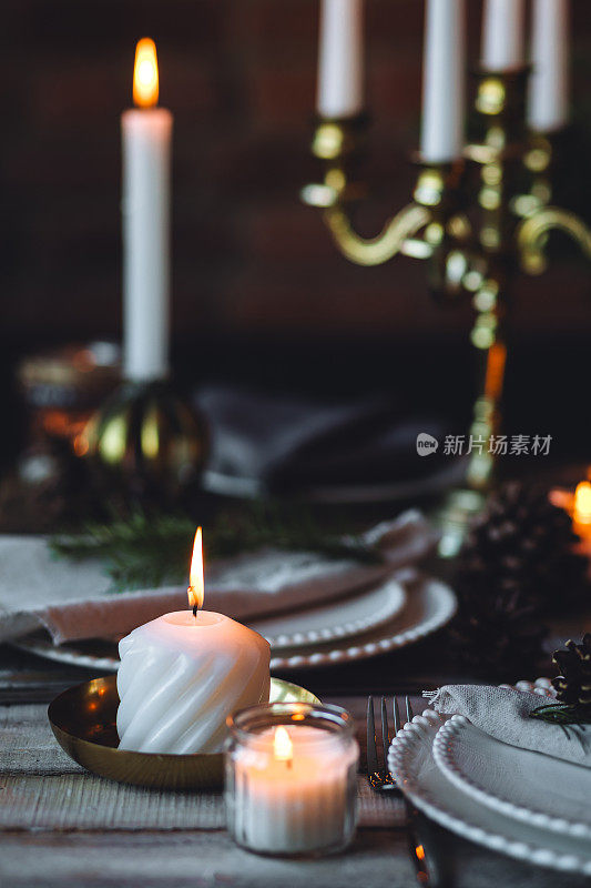 为家庭圣诞晚餐准备的漂亮的餐桌摆设。温馨的气氛，烛光。葡萄酒杯，复古吊灯，优雅的内饰。杉木树枝，木质家具，暗色调，散景