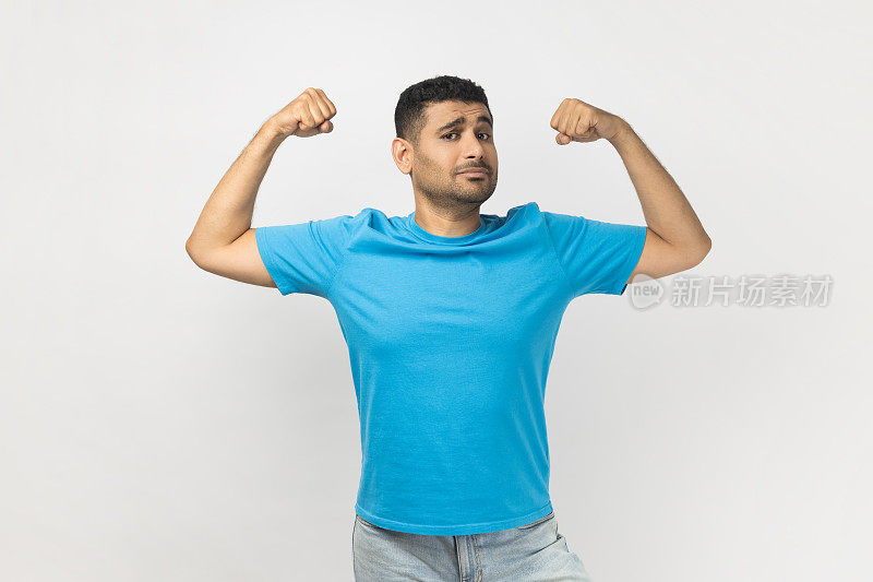 站着的自信强壮有力的没刮胡子的男人举起双臂，展示着他的肱二头肌和力量。