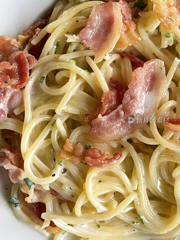 全画幅的意大利面，以培根、帕尔马干酪、切碎的大蒜、鸡蛋为特色的意大利面，放在白色盘子上，高架视图