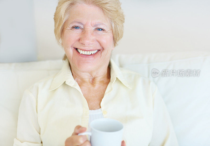 坐在沙发上喝着咖啡的快乐老妇人
