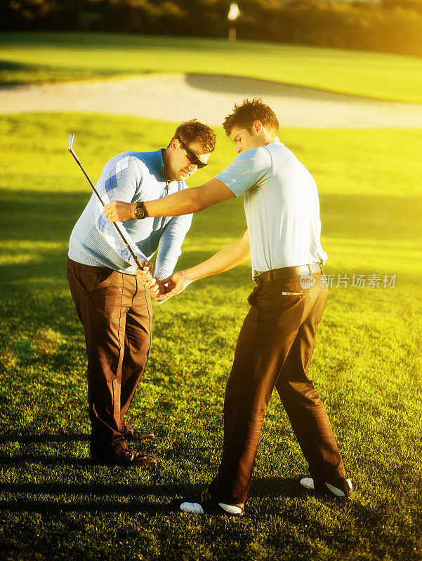 年轻的高尔夫教练纠正高尔夫球手在阳光明媚的球场上挥杆