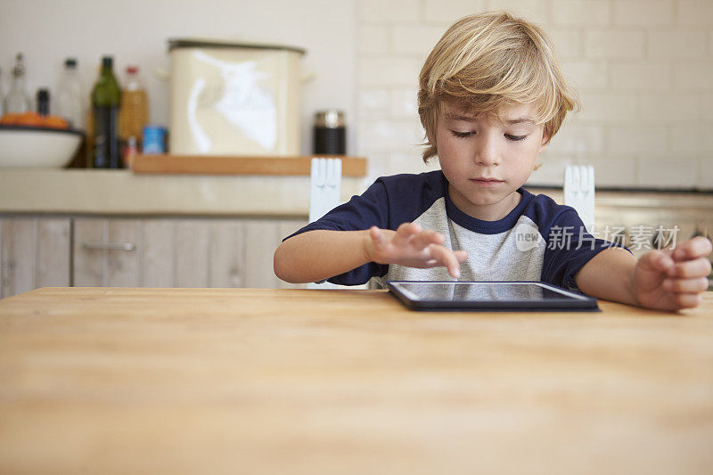 小男孩在餐桌上使用平板电脑，正面