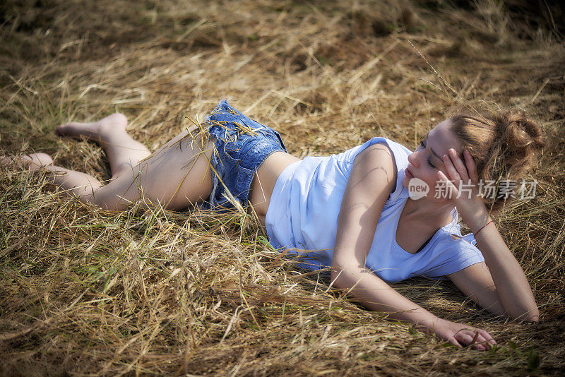 年轻的金发女郎躺在地里干稻草上
