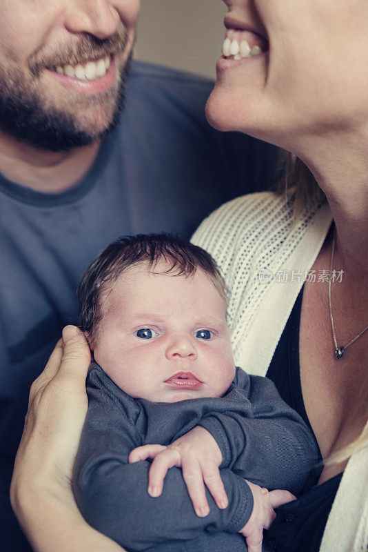 新父母抱着新生婴儿微笑，特写垂直。