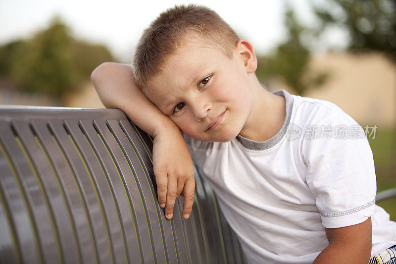 悲伤的小男孩独自坐在长凳上