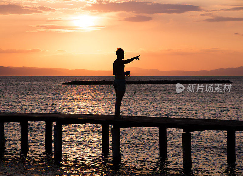 日落时分，在土耳其阿瓦利克巴利克希尔附近的爱琴海海岸码头上的一个人