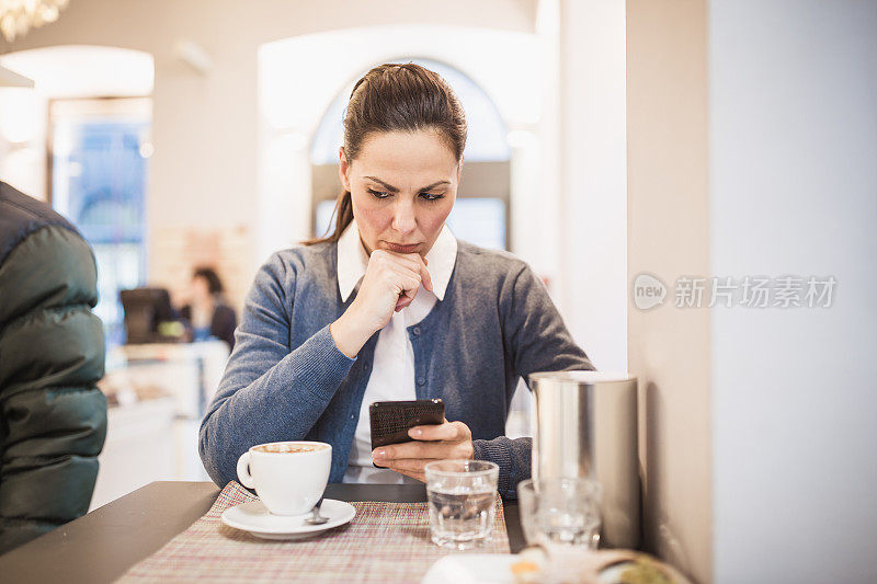 可爱的女人喝着咖啡，用着手机，坐在咖啡里