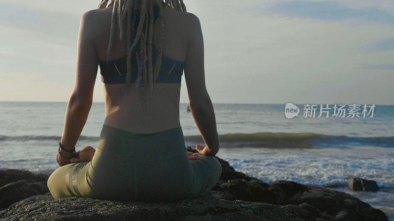 日落时做瑜伽。一个年轻女子在沙滩上冥想莲花姿势
