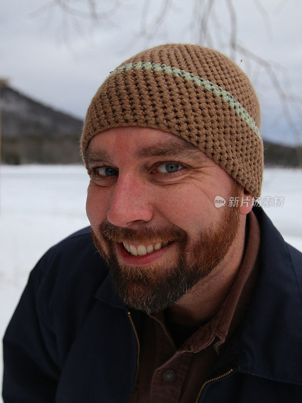 有胡子的蓝眼睛，漂亮的牙齿，微笑的人戴钩针编织的冬季帽子