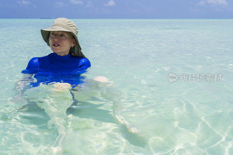 年长妇女享受坐在浅水在小岛屿海滩在四月，马尔代夫