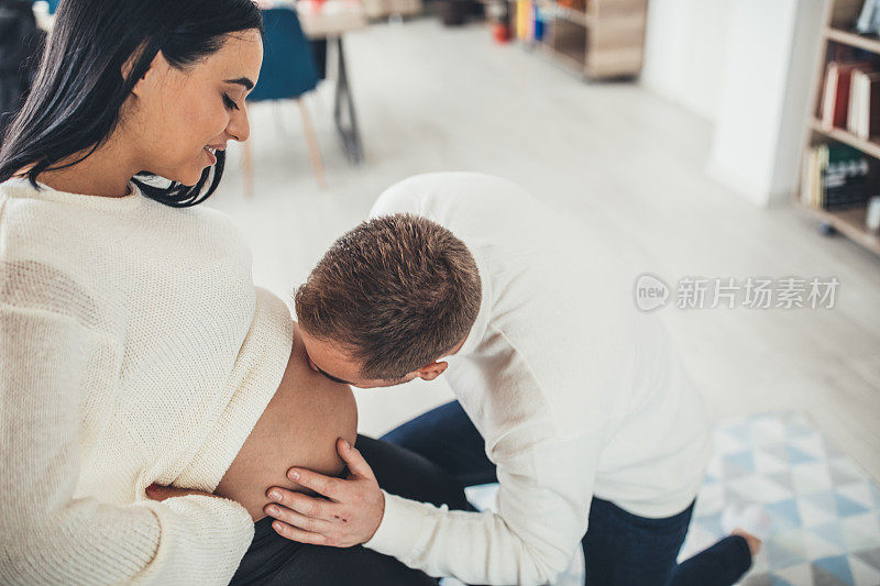 丈夫通过女人的肚子亲吻新生儿